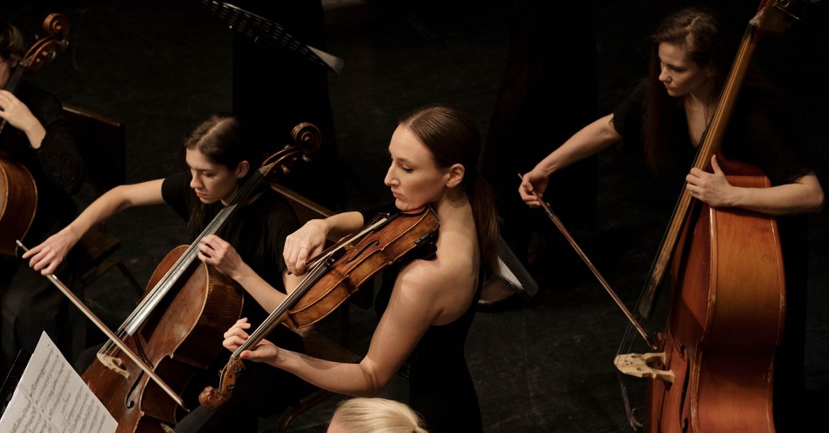 A group of female musicians playing string instruments during an indoor concert.